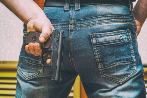 A man in jeans holding a gun in his hand behind his back
